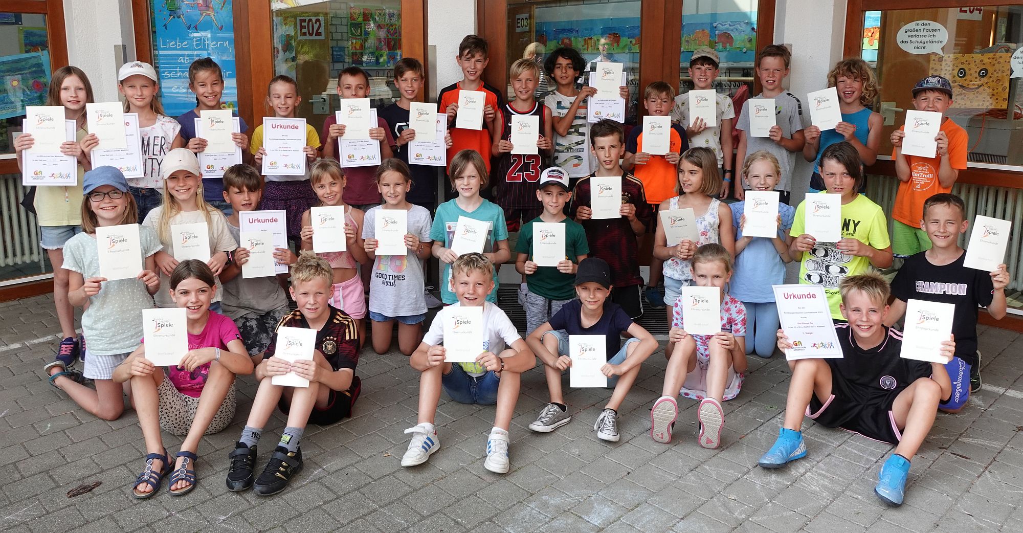 Kinder mit ihren Urkunden vor dem Schulgebäude